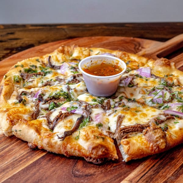 MOMO Craft Pizza's sliced pizza with melted cheese, red onions, and herbs, served with dipping sauce.