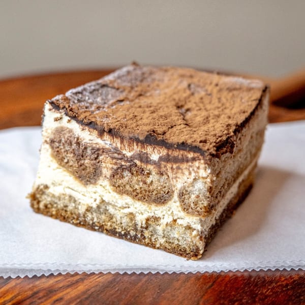 A slice of tiramisu dessert with layers of cream and coffee-soaked cake, dusted with cocoa.