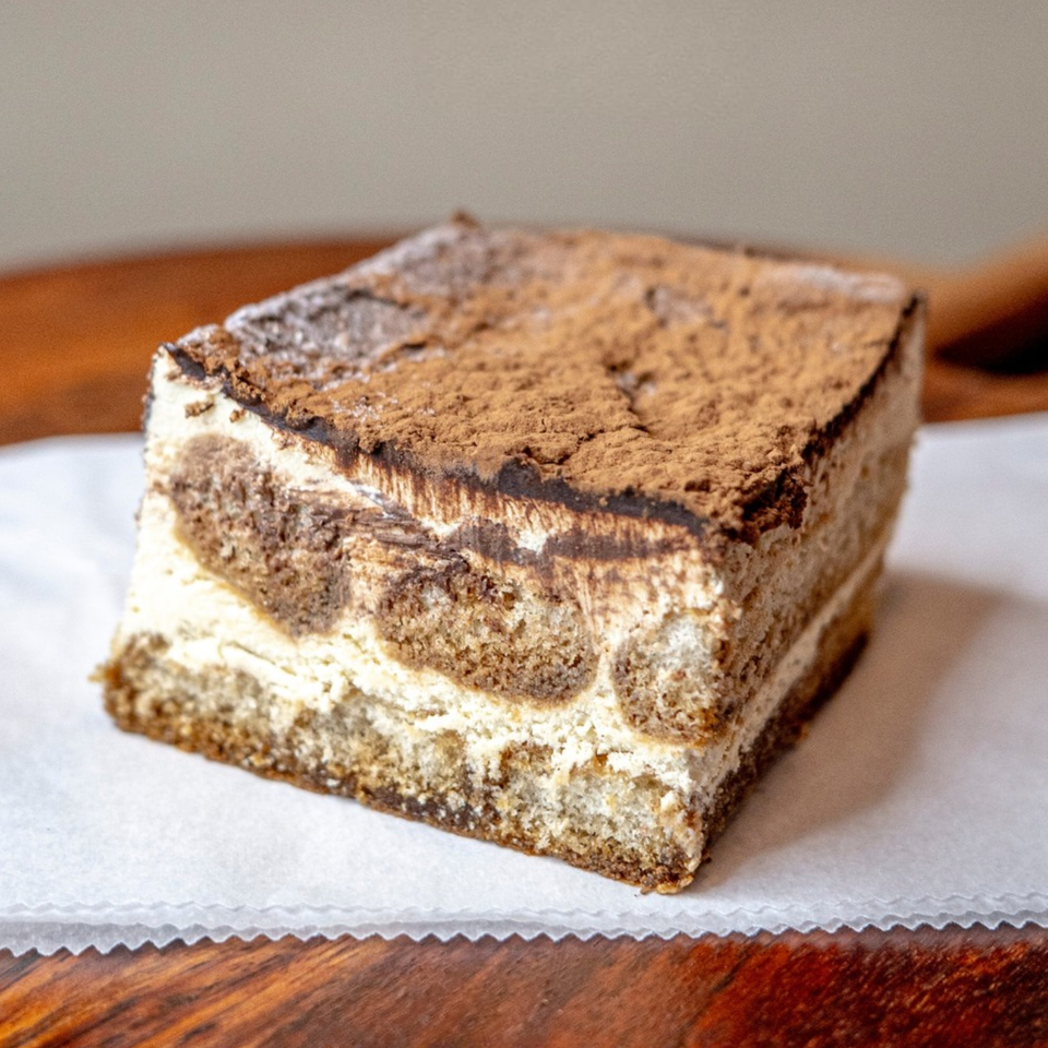 A slice of tiramisu dessert with layers of cream and coffee-soaked cake, dusted with cocoa.
