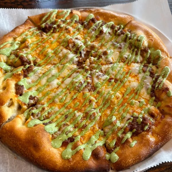 MOMO Craft Pizza with melted cheese, ground meat, and a vibrant green sauce drizzled on top.