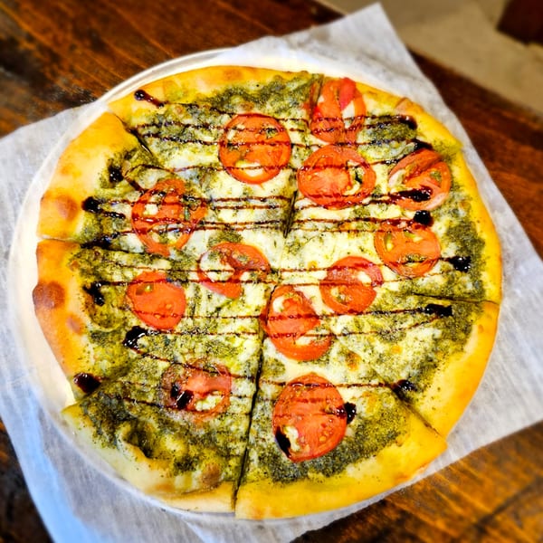 MOMO Craft Pizza's pesto pizza with sliced tomatoes and balsamic glaze on parchment paper.