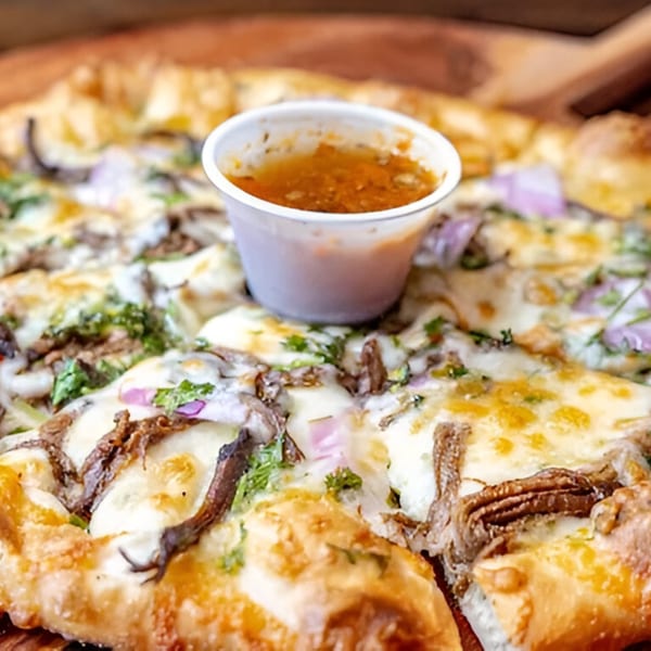 MOMO Craft Pizza with melted cheese, red onions, and cilantro, served with a side of dipping sauce.